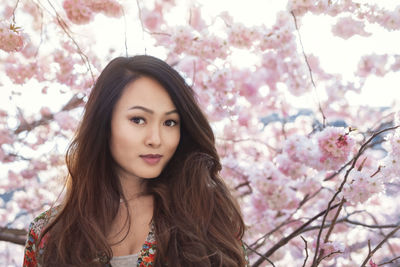 Portrait of young woman standing against tree