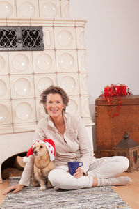 Portrait of woman with dog sitting by fireplace at home during christmas