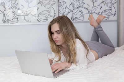 Young woman using mobile phone while sitting on bed