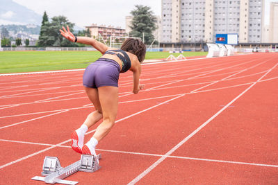 Full body back view of determined young female sprinter starting to run from blocks on track of stadium