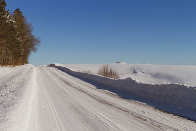 Road amidst snow covered land against clear blue sky