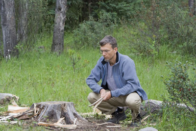 Mature man crouching by tree stump on field at forest