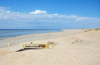 Abandoned piano at beach against sky