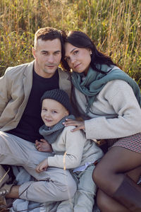 Family of three with a boy child mom and dad are sit on a field in autumn at sunset