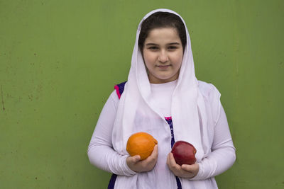 Portrait of man holding fruit against orange wall