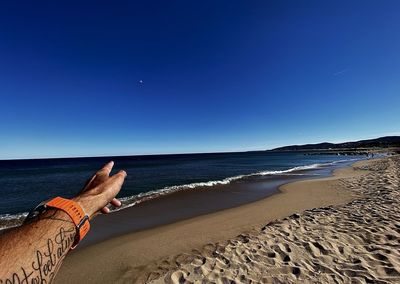 Low section of people on beach against clear blue sky