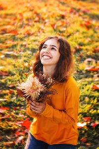 Curly young girl in yellow sweater on the grass with autumn bouquet of dry leaves and flowers