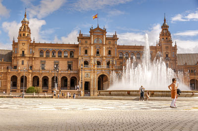 People at fountain in city against sky