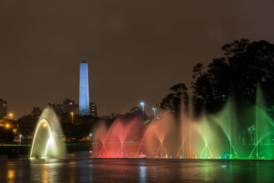 Illuminated fountain by building against sky at night