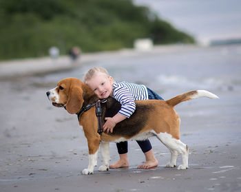 Portrait of girl embracing dog while standing at beach