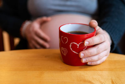 Midsection of pregnant woman with coffee cup on table