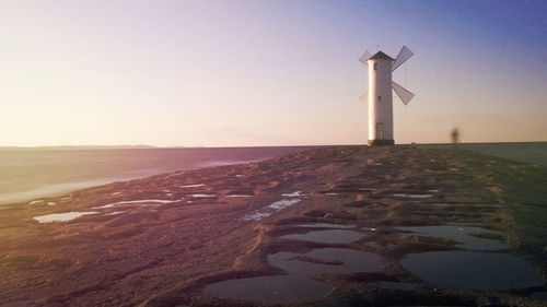 Lighthouse by sea against clear sky