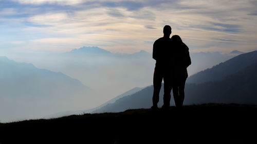Rear view of silhouette couple standing on mountain against sky