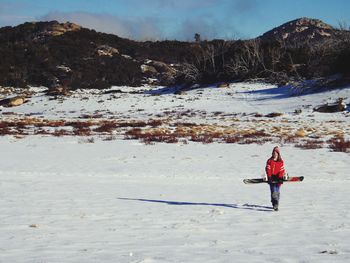 Full length of girl carrying skies while walking on snow covered land