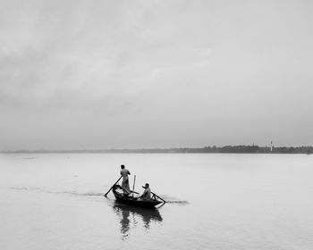 People rowing boat in sea against sky