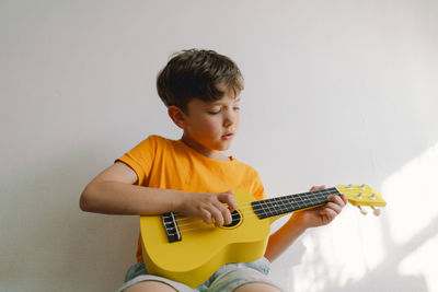 Cute boy learns to play the yellow ukulele guitar in home. cozy home.