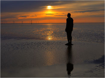 Silhouette man walking on beach against sky during sunset