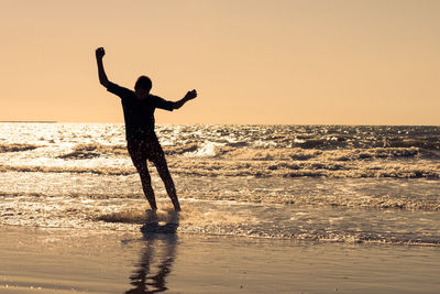 Silhouette man standing in sea against clear sky during sunset