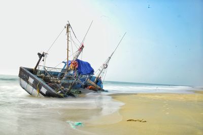 Fallen fishing ship at beach against clear sky
