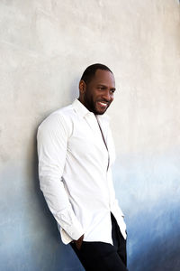 Handsome cheerful african american man in white shirt standing by grey blue textured wall.