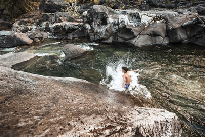 Hiker enjoying in river against rocks at forest