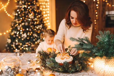 Mo and daughter in sweaters together prepare a festive cake for the christmas holiday in the kitchen