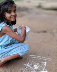 Portrait of smiling girl making rangoli while sitting on land