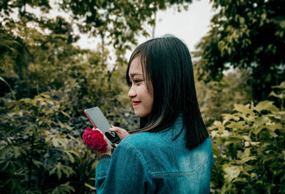 Young woman using phone while standing on plants