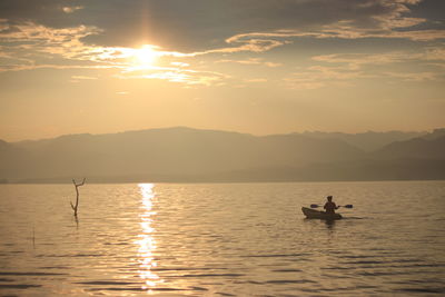 Silhouette people on boat in lake against sky during sunset
