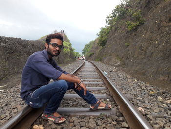 Portrait of young man sitting on railroad track amidst rock formation