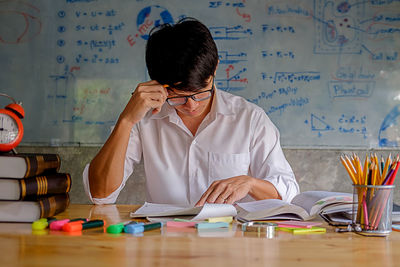 Young man studying with school supplies on table at home