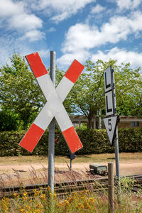 Road sign by trees on field against sky