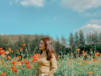Beautiful woman standing in field with flowers against sky