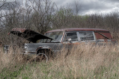 Abandoned car on field against sky