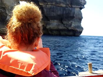 Rear view of woman wearing life jacket in boat on sea