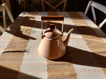 A cream colored teapot on the tablecloth in the morning time