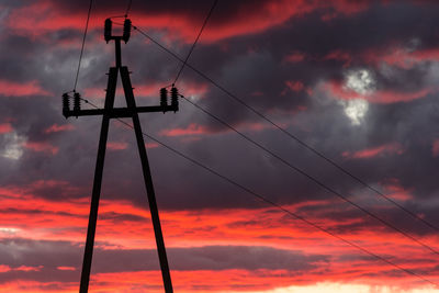 Low angle view of silhouette electricity pylon against dramatic sky during sunset