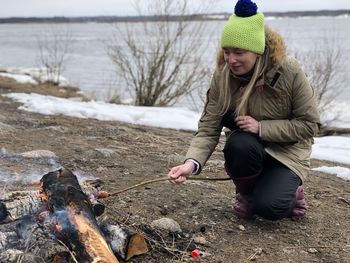 A woman on a picnic fries a sausage on a fire.