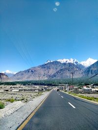 Road leading towards mountains against clear blue sky