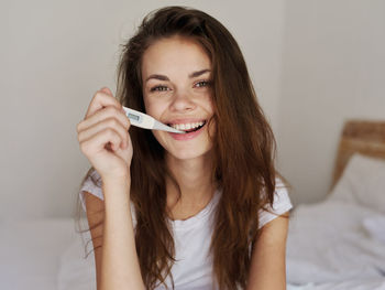 Portrait of smiling young woman holding while relaxing on bed at home