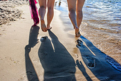 Low section of women walking on shore at beach