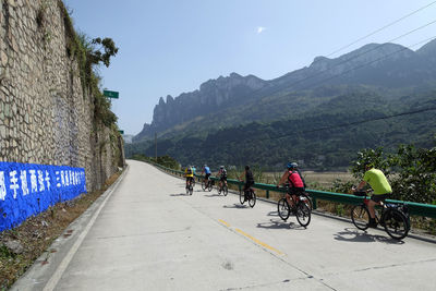People riding bicycle on road by mountains against sky