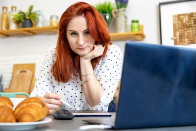 Woman using laptop while sitting at home. young woman sitting in kitchen and working on laptop.