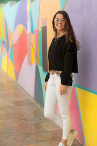 Portrait of smiling young woman standing against colorful wall