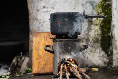 Pressure cooker kept on top of a modern chulah with wood being burnt.