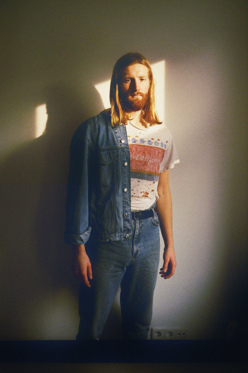 PORTRAIT OF YOUNG MAN LOOKING AWAY WHILE STANDING AGAINST WALL