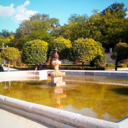 Fountain in park by lake against sky