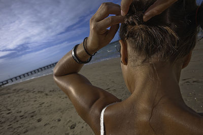 Rear view of woman tying hair at beach