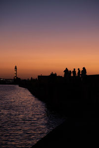 Silhouette people at sunset with a lighthouse in the background 