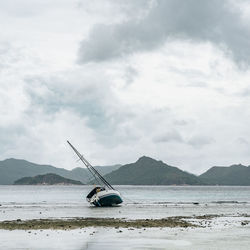 Sailboat moored at beach against cloudy sky